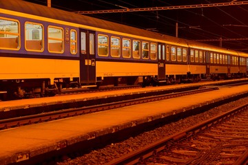 Fototapeta na wymiar White and blue train standing at a small roofless train station at night in the Czech Republic. European train
