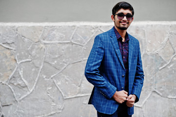 Young indian man on blue suit and sunglasses posed outdoor.