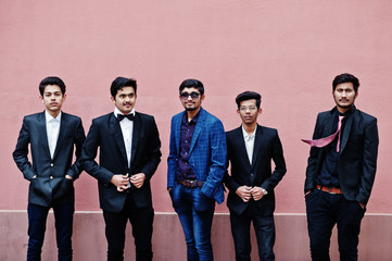 Group of 5 indian students in suits posed outdoor against pink wall.