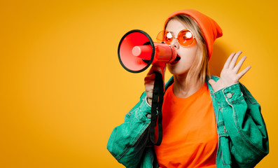Young style girl in jeans clothes with pink megaphone on yellow background. Symbolizes female resistance. Clothes in 1980s style - obrazy, fototapety, plakaty