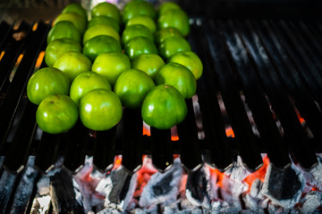 Tomates verdes asandose en la parrila del asador al carbon