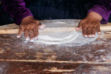 Woman's hands rolling out a dough with rolling pin on the shabby wooden table