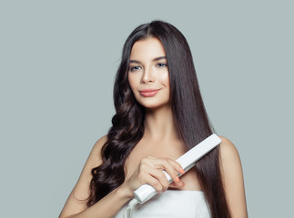 Beautiful woman with long straight hair and curly hair using hair straightener. Cute smiling girl straightening healthy brunette hairstyle with flat iron. Hair problem and haircare concept
