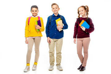 schoolchildren with backpacks and multicolored books looking at camera isolated on white