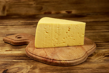 Piece of cheese on cutting board on wooden table