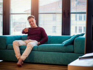Fototapeta premium Young man sitting watching television changing the channel with the remote control