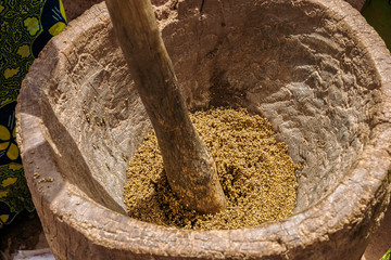 Close-up of a woman crushing cereals like millet with a wooden mortar and pestle, West Africa,...