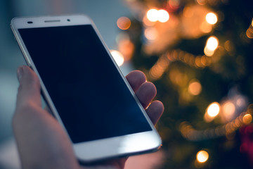 man with smartphone mobile for social network internet with merry christmas light of tree