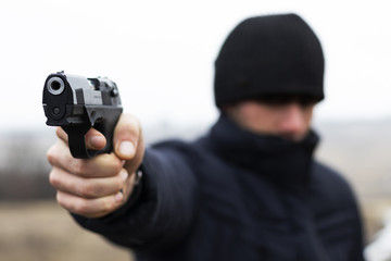 Young robber shoots a pistol close-up, crime concept