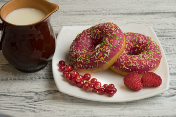 Donuts with icing, berries and milk jug on white wooden background