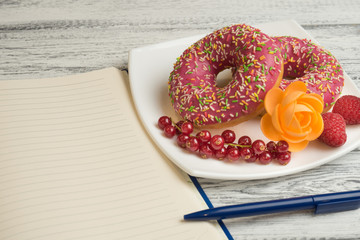 Donuts with icing and berries on the plate Next to lies a notebook to record the recipes of donuts