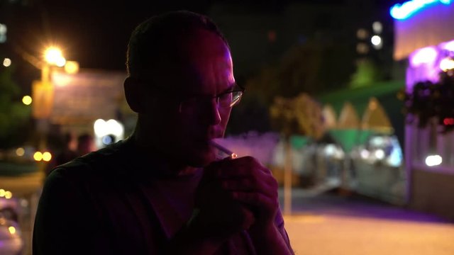 Middle-aged man lighting a cigarette in a city street at night in summer 