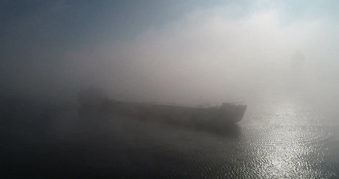 A huge barge on the river Dnipro in the morning fog with a visible silhouette of the buildings and city in the background (shot from the air) in 4K 4