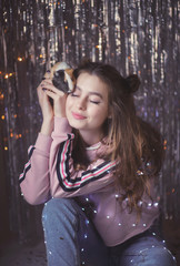 Fototapeta premium gentle and beautiful young girl on the background of garlands and tinsel with Guinea pig