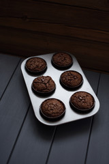 Minimalist style homemade pastry. Chocolate muffins with chocolate chips in metal baking tray on dark background