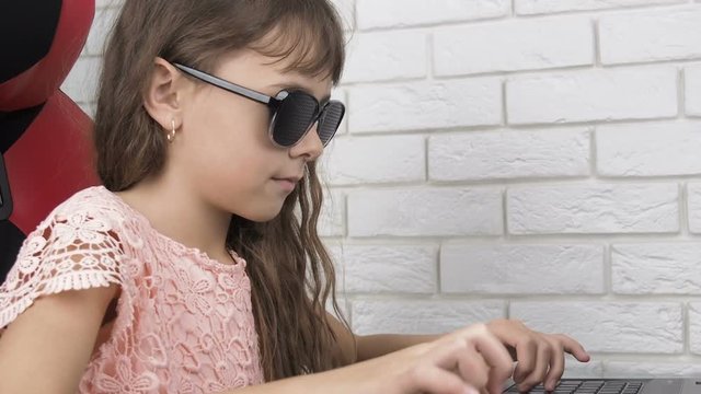 Child typing on laptop. Little girl in obscura glasses works on a laptop.