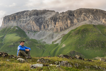 Young man in blue sportswear sits on a hill on a background of rocky mountains