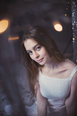 delicate and beautiful young girl in white dress on the background of garlands and tinsel