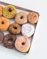 Assorted gourmet donuts on a tray. Sweet and delicious doughnuts made with chocolate, vanilla, frosting, and powdered sugar. 