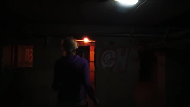 Woman running away from pursuer in dark gloomy basement corridor