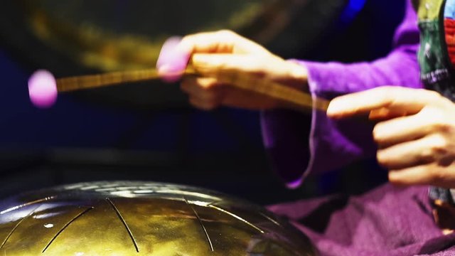 Woman is playing meditative instrument tank drum in a dark meditation room. Close-up