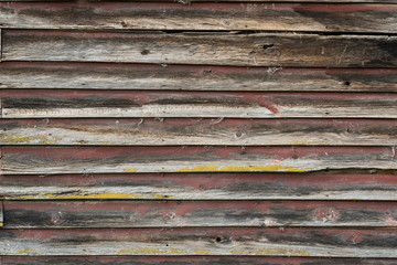 The side wall of an old, derelict, wooden barn with yellow lichen and the remnants of dark, red...