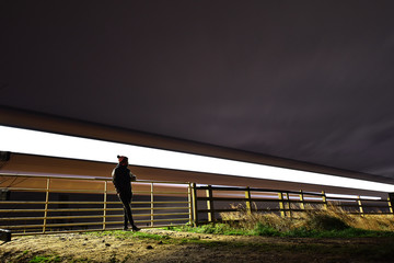 abstract long exposure of person leaning on gate with train passing behind 