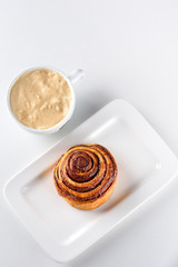 Perfect morning,sweet breakfast and start day.Coffee cup and Cinnamon Danish Swirl-classic buttery danish pastry rolled with cinnamon and glazed with sugar on dish on white background.