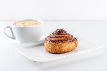 Perfect morning,sweet breakfast and start day.Coffee cup and Cinnamon Danish Swirl-classic buttery danish pastry rolled with cinnamon and glazed with sugar on dish on white background.
