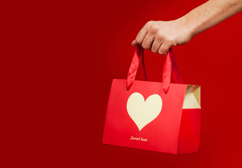 A girl holds a gift with a heart closeup on an isolated red background. Valentine day concept.