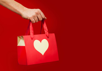 A girl holds a gift with a heart closeup on an isolated red background. Valentine day concept.