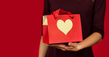 A girl holds a gift with a heart closeup on an isolated red background. Valentine day concept.