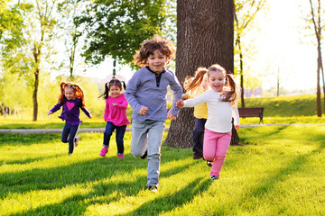 a group of small happy children run through the park in the background of grass and trees....