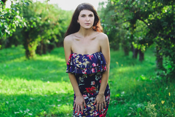 Young beautiful brunette girl in a blue dress in the summer park on the background of green grass