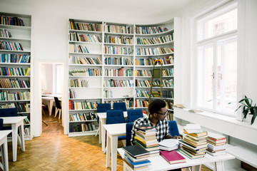 Portrait of african university student visiting library, reads book attentively, studies business terms before changing job .