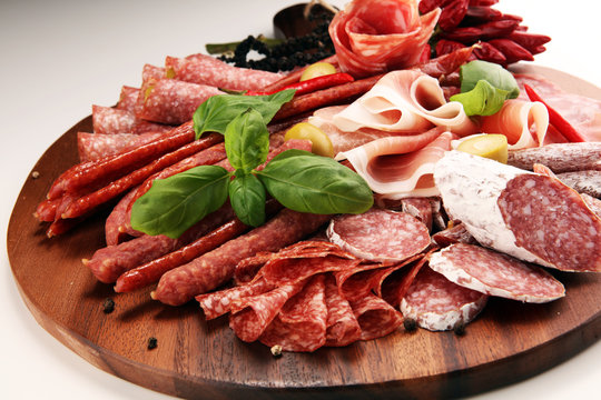 Food tray with delicious salami, pieces of sliced prosciutto crudo, sausage and basil. Meat platter with selection