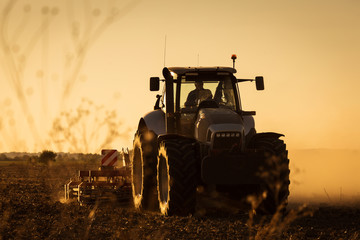 Modern tractor plowing at the sunset with lot of dust in background © danmir12