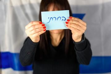 Young Woman Holding Ballot Front Of Face on Israeli Flag Background.Hebrew text I Voted on voting paper.