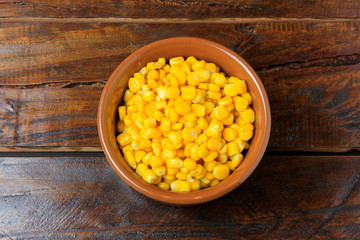 Raw corn kernels inside ceramic pot on rustic wooden table. space for text