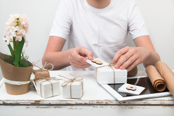 Teen boy wrapping boxes with gifts for his mother, grandmother and sister to congratulate them on Women's Day on March 8, Mother's Day, Happy Valentine's Day.