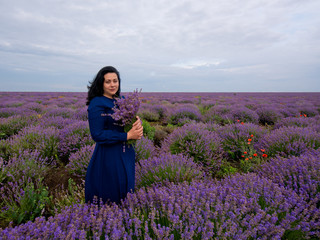 Young girl with a bouquet in hands, posing in a lavender field.