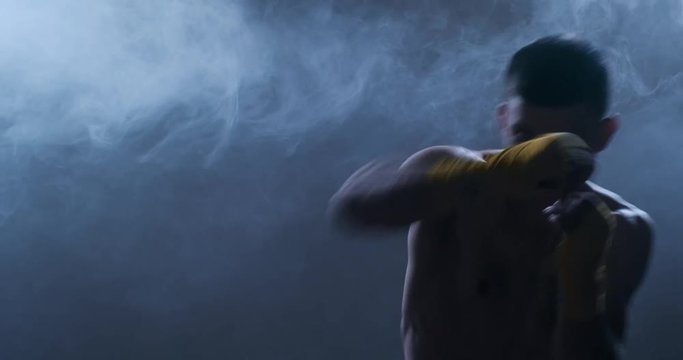 Muscular man in yellow gloves shows the different movements and strikes in the studio. Fog in the background