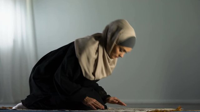 Kneeling arab woman prostrating on islamic praying rug, religious worship, faith