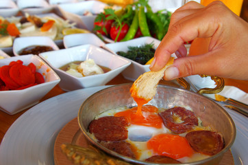 A hand dipping bread to fried eggs with Turkish sausage plate