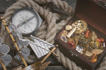 Pirate ship, treasure map, treasure chest full of gold and a compass on a wooden table background.