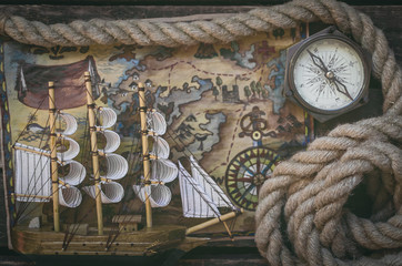 Fototapeta na wymiar Pirate ship, treasure map, compass and a mooring rope on a wooden table background.