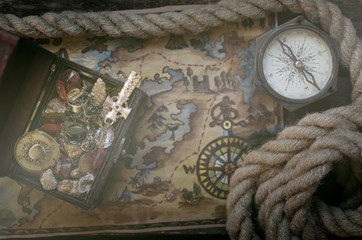 Fototapeta na wymiar Pirate treasure map, treasure chest full of gold, compass and a mooring rope on a wooden table background.