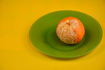 Slightly peeled mandarin on a green plate on a yellow background.