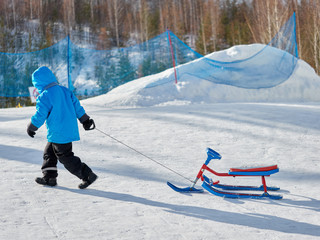 A boy in the winter carries a snow scooter uphill on pure white snow.