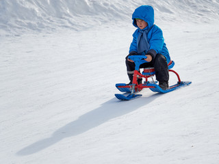 Fototapeta na wymiar Boy in winter sledge rides on the mountain